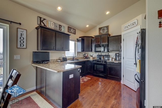 kitchen with a peninsula, dark wood-type flooring, a sink, light stone countertops, and black appliances