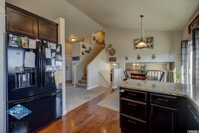 kitchen with dark brown cabinetry, black fridge with ice dispenser, wood finished floors, light stone countertops, and vaulted ceiling