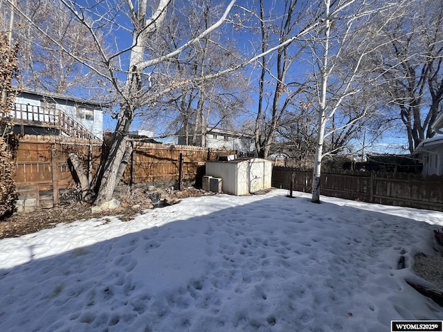 yard layered in snow featuring a storage shed, an outdoor structure, and a fenced backyard