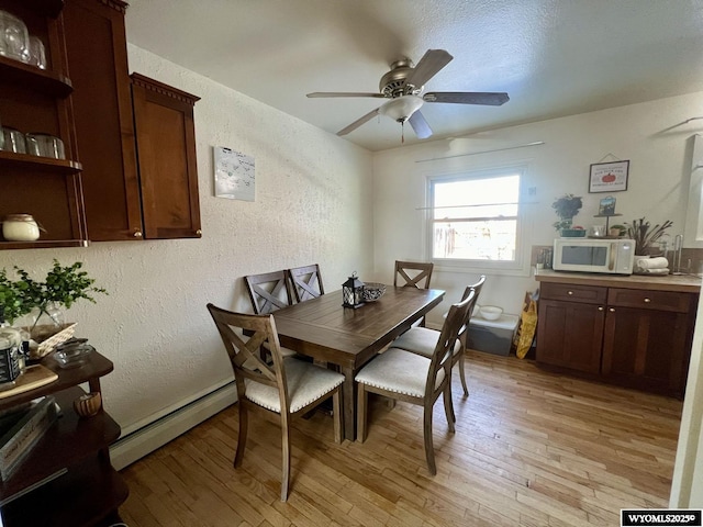 dining room featuring a baseboard heating unit, a textured wall, ceiling fan, and light wood-type flooring