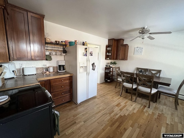 kitchen with dark countertops, open shelves, white refrigerator with ice dispenser, and light wood-type flooring