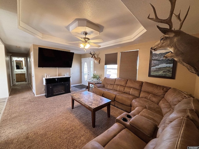 living area featuring baseboards, a raised ceiling, a ceiling fan, carpet floors, and a fireplace