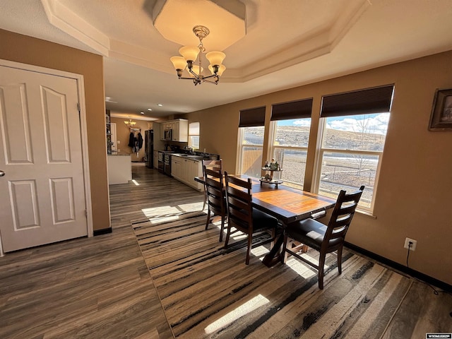 dining space featuring a chandelier, a tray ceiling, dark wood-style floors, and baseboards