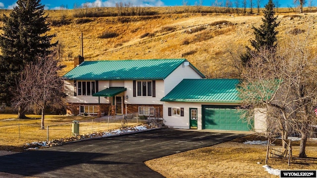 bi-level home with aphalt driveway, metal roof, fence, and a chimney