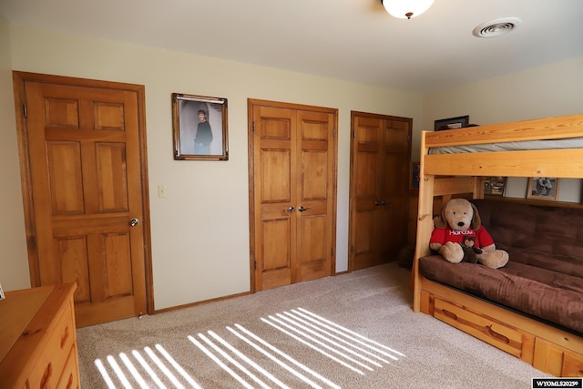 bedroom featuring visible vents, light carpet, baseboards, and two closets