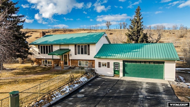 bi-level home featuring driveway, metal roof, an attached garage, fence, and brick siding