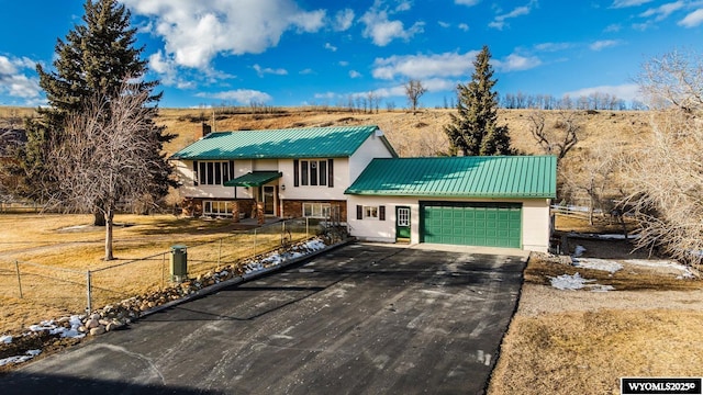 raised ranch featuring a garage, driveway, metal roof, and fence