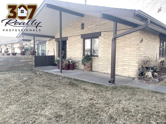 view of side of home featuring a yard, fence, a patio, and brick siding