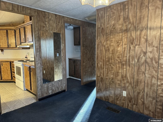 kitchen with brown cabinets, under cabinet range hood, light countertops, wood walls, and white range with electric cooktop