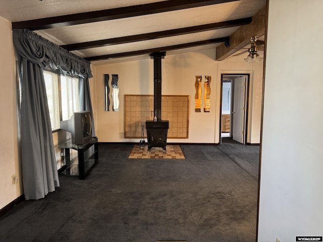 unfurnished living room with dark colored carpet, a wood stove, vaulted ceiling with beams, and baseboards