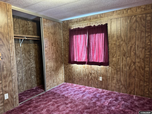 unfurnished bedroom featuring a closet, carpet flooring, wooden walls, and a textured ceiling