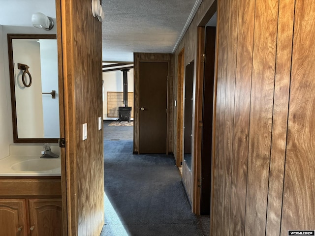 corridor featuring a textured ceiling, dark carpet, and a sink