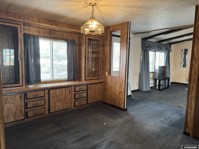 unfurnished dining area featuring wood walls, baseboards, and dark colored carpet