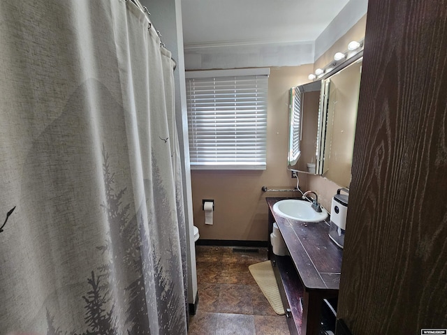 bathroom with toilet, stone finish floor, baseboards, and vanity