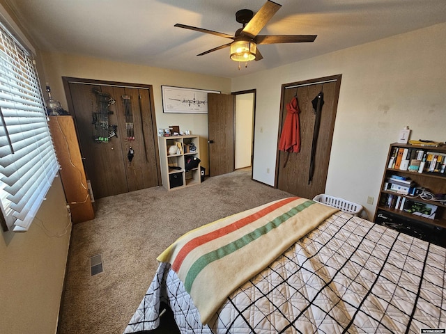 carpeted bedroom featuring ceiling fan, visible vents, and multiple closets