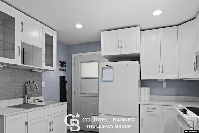 kitchen featuring white appliances, a sink, white cabinetry, light countertops, and glass insert cabinets