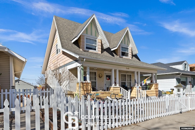 view of front of home featuring roof with shingles, a porch, and a fenced front yard