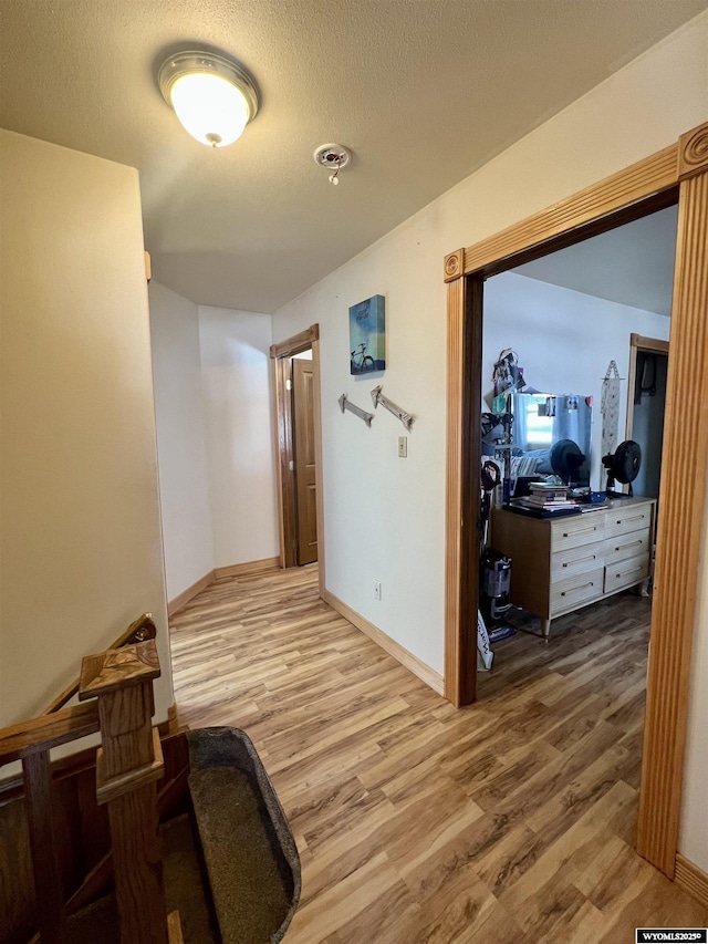 corridor with light wood-style floors, a textured ceiling, and baseboards