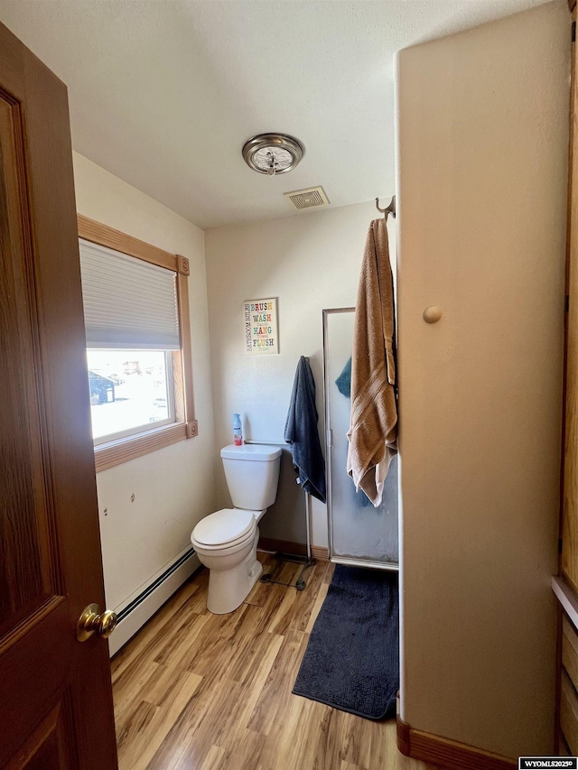 bathroom with toilet, a baseboard heating unit, wood finished floors, visible vents, and baseboards