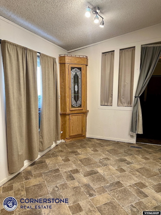 empty room with stone finish flooring, ornamental molding, and a textured ceiling