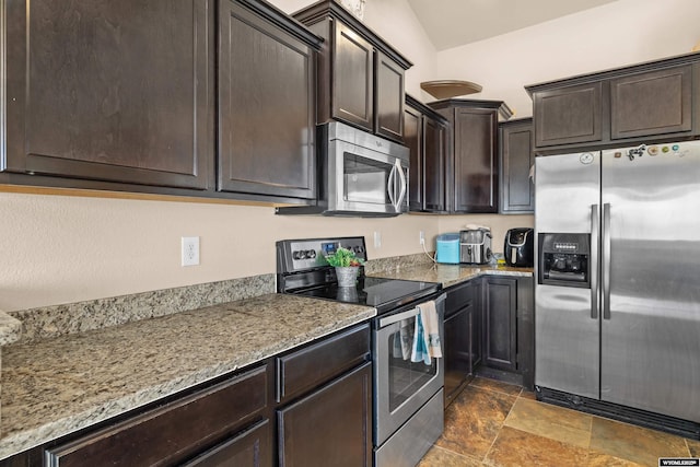 kitchen featuring light stone counters, stone finish flooring, vaulted ceiling, stainless steel appliances, and dark brown cabinets