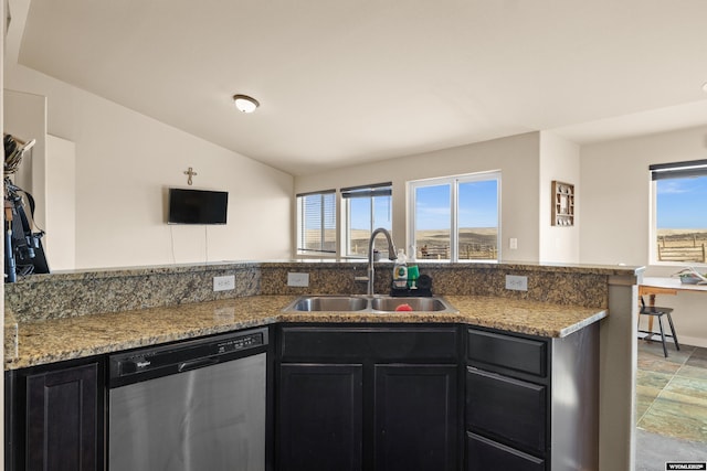 kitchen featuring lofted ceiling, dark cabinets, a sink, stainless steel dishwasher, and light stone countertops