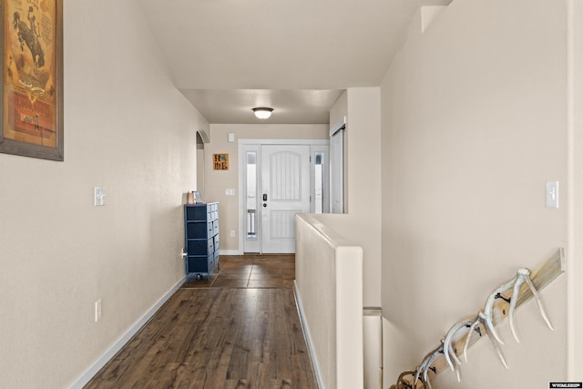 hallway with dark wood-type flooring, arched walkways, and baseboards