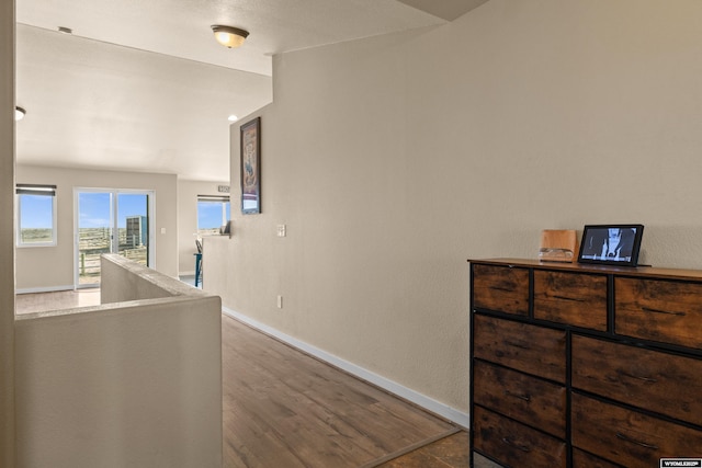 corridor with baseboards, wood finished floors, and an upstairs landing