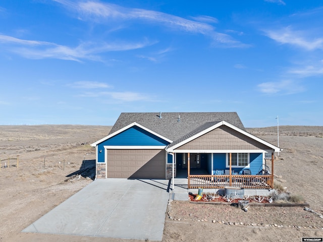 view of front of home with roof with shingles, covered porch, a garage, stone siding, and driveway