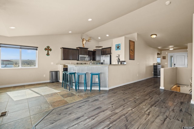 kitchen with baseboards, appliances with stainless steel finishes, vaulted ceiling, dark brown cabinets, and light countertops