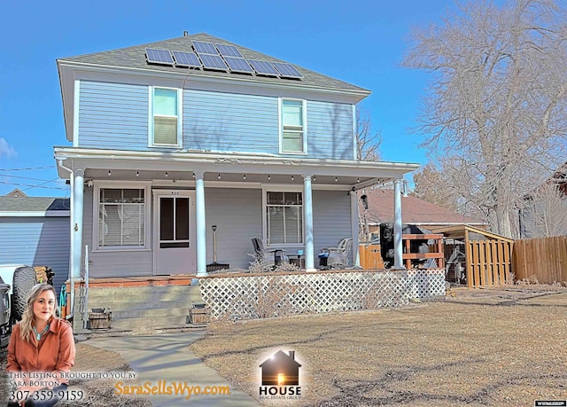 view of front of property with a porch, fence, and roof mounted solar panels