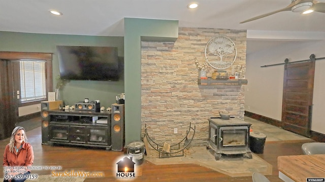 living room with a barn door, wood finished floors, a ceiling fan, baseboards, and a wood stove