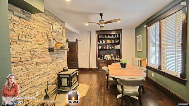 dining area featuring radiator, a barn door, a ceiling fan, dark wood-type flooring, and baseboards