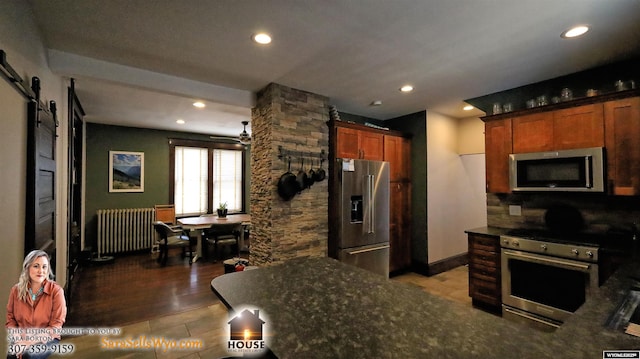 kitchen with stainless steel appliances, dark countertops, radiator, recessed lighting, and a barn door