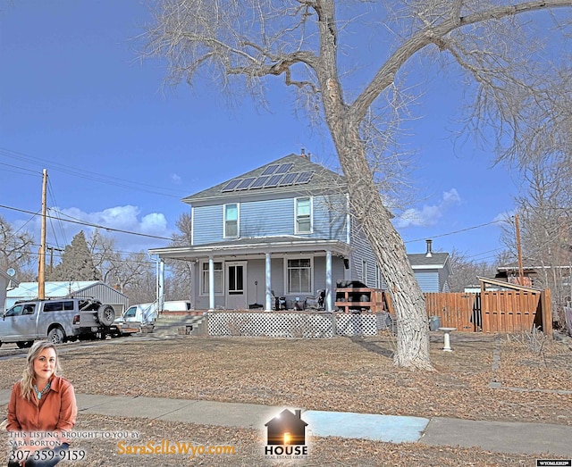 view of front facade featuring roof mounted solar panels, a porch, and fence