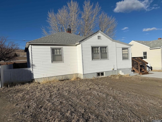 exterior space with a shingled roof, a chimney, and fence