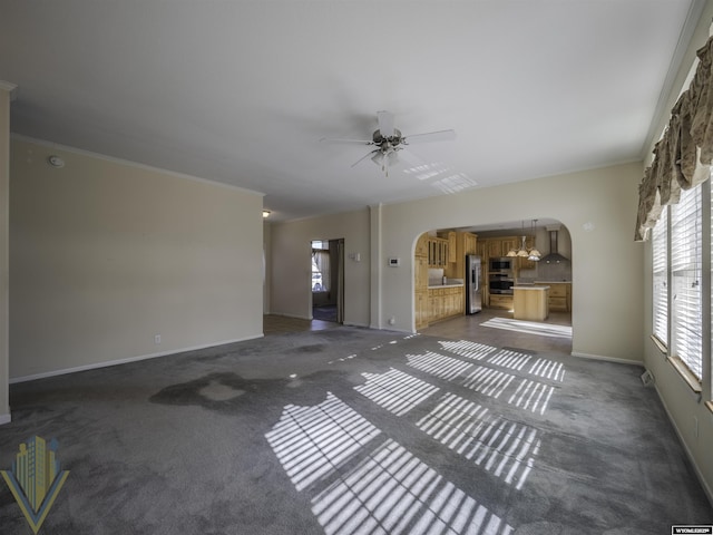 unfurnished living room featuring arched walkways, dark carpet, a ceiling fan, and crown molding