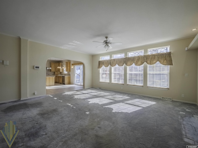 unfurnished living room with arched walkways, ceiling fan, carpet flooring, visible vents, and crown molding