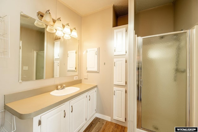 bathroom with wood finished floors, visible vents, vanity, ornamental molding, and a stall shower