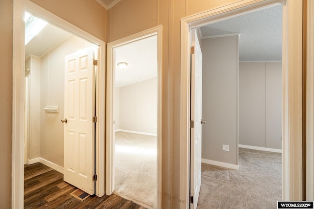 hallway with baseboards, ornamental molding, dark carpet, and dark wood-type flooring