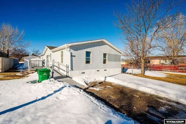 view of snowy exterior with crawl space, fence, and a deck