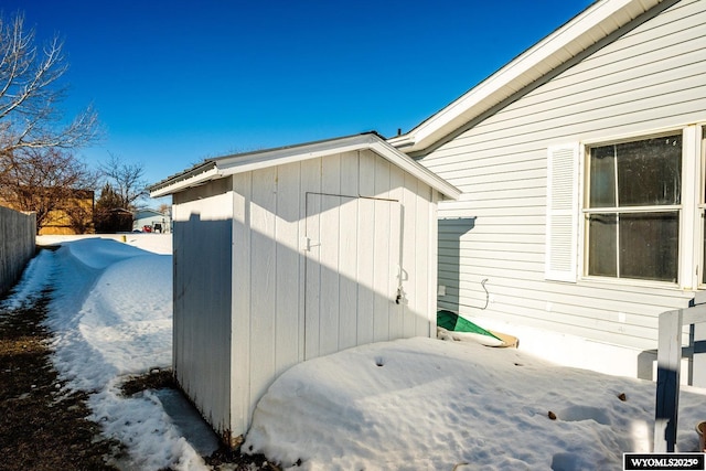 view of snowy exterior featuring an outbuilding, fence, and a storage shed