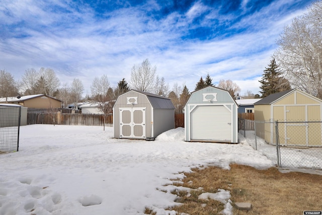 snow covered structure with an outbuilding, fence, and a storage unit