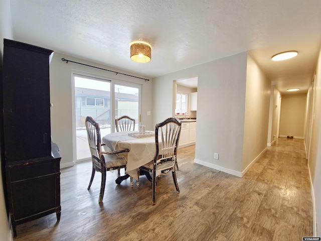 dining area with light wood-style floors, baseboards, and a textured ceiling