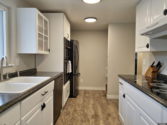 kitchen featuring black electric stovetop, under cabinet range hood, wood finished floors, a sink, and freestanding refrigerator