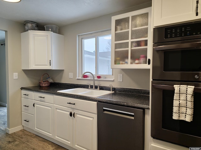 kitchen featuring dishwashing machine, a sink, white cabinets, multiple ovens, and dark countertops