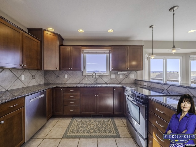 kitchen with light tile patterned flooring, a sink, appliances with stainless steel finishes, dark stone counters, and tasteful backsplash