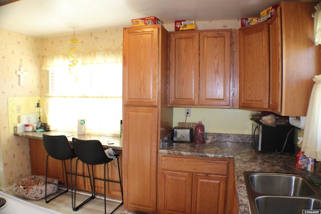 kitchen featuring dark countertops, wallpapered walls, brown cabinets, and a sink