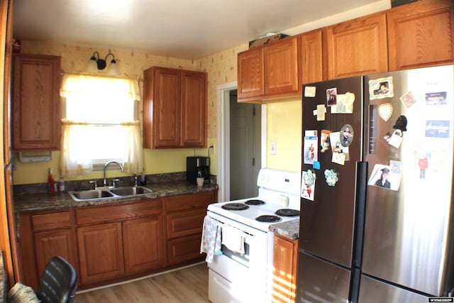 kitchen featuring white electric range, a sink, freestanding refrigerator, brown cabinetry, and wallpapered walls