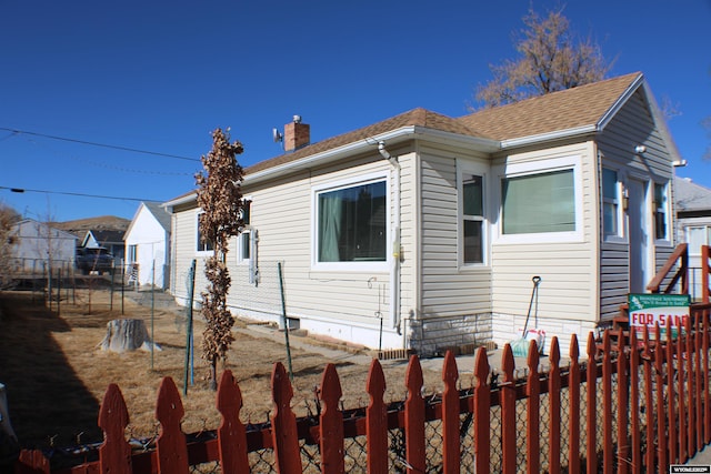 view of front of house with a shingled roof, a chimney, and fence